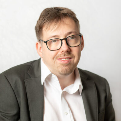 Mann mit kurzem, braunem Haar. Er trägt Anzug und eine Brille.