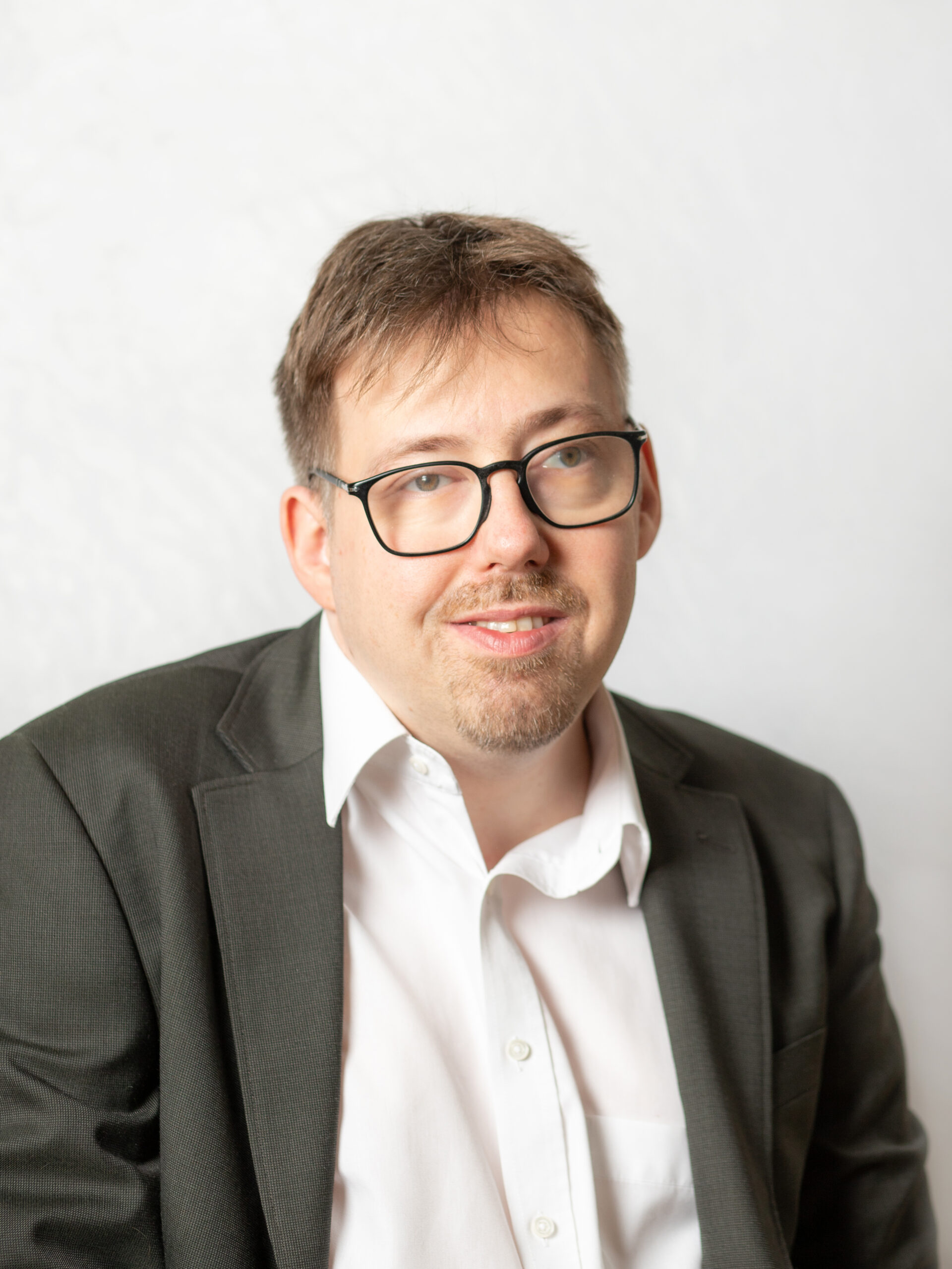 Mann mit kurzem, braunem Haar. Er trägt Anzug und eine Brille.