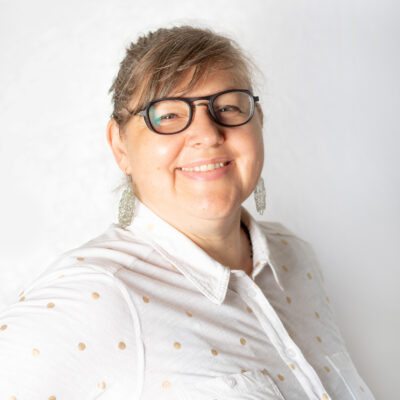 Frau mit zusammengebundenem, blondem Haar und Brille.
