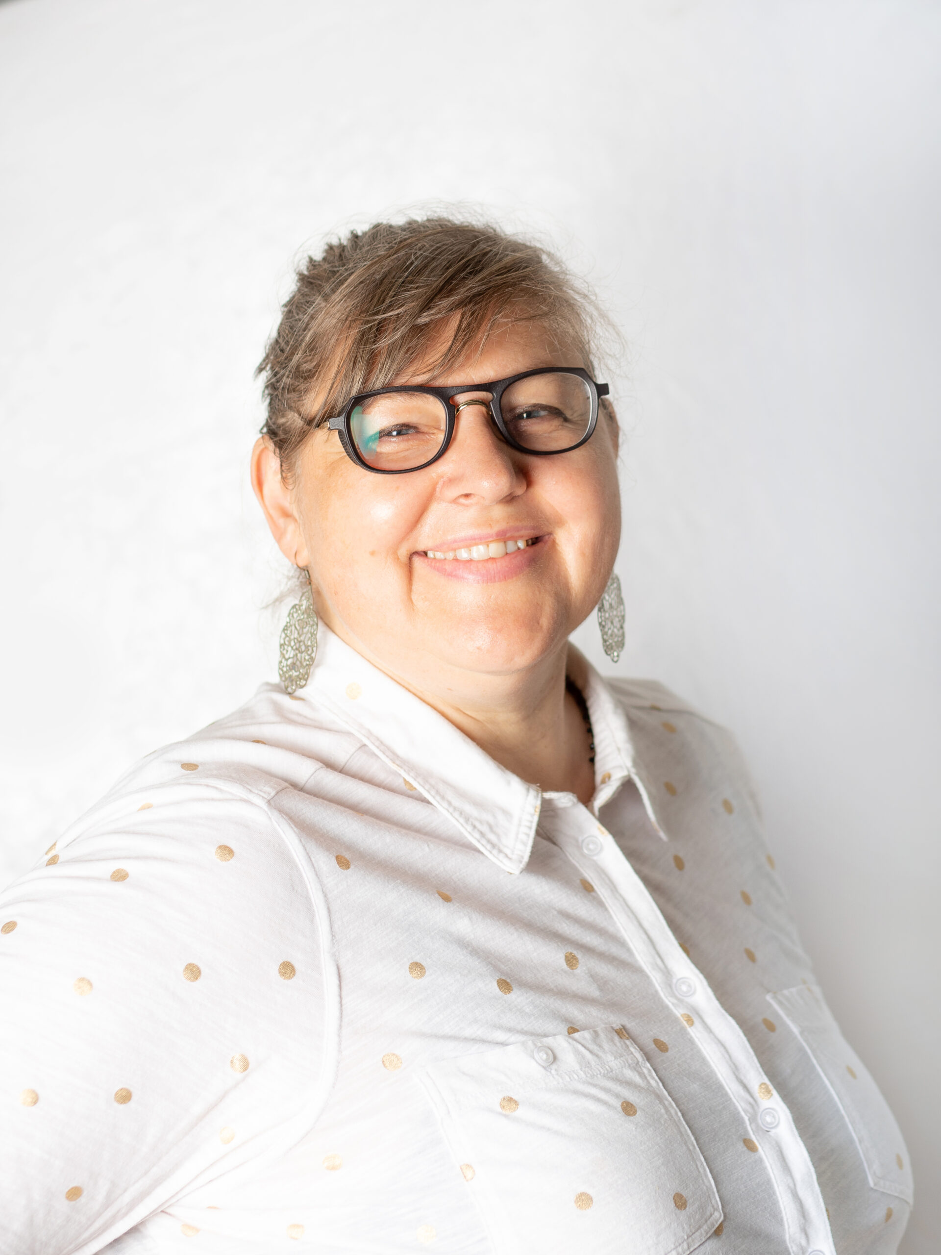 Frau mit zusammengebundenem, blondem Haar und Brille.