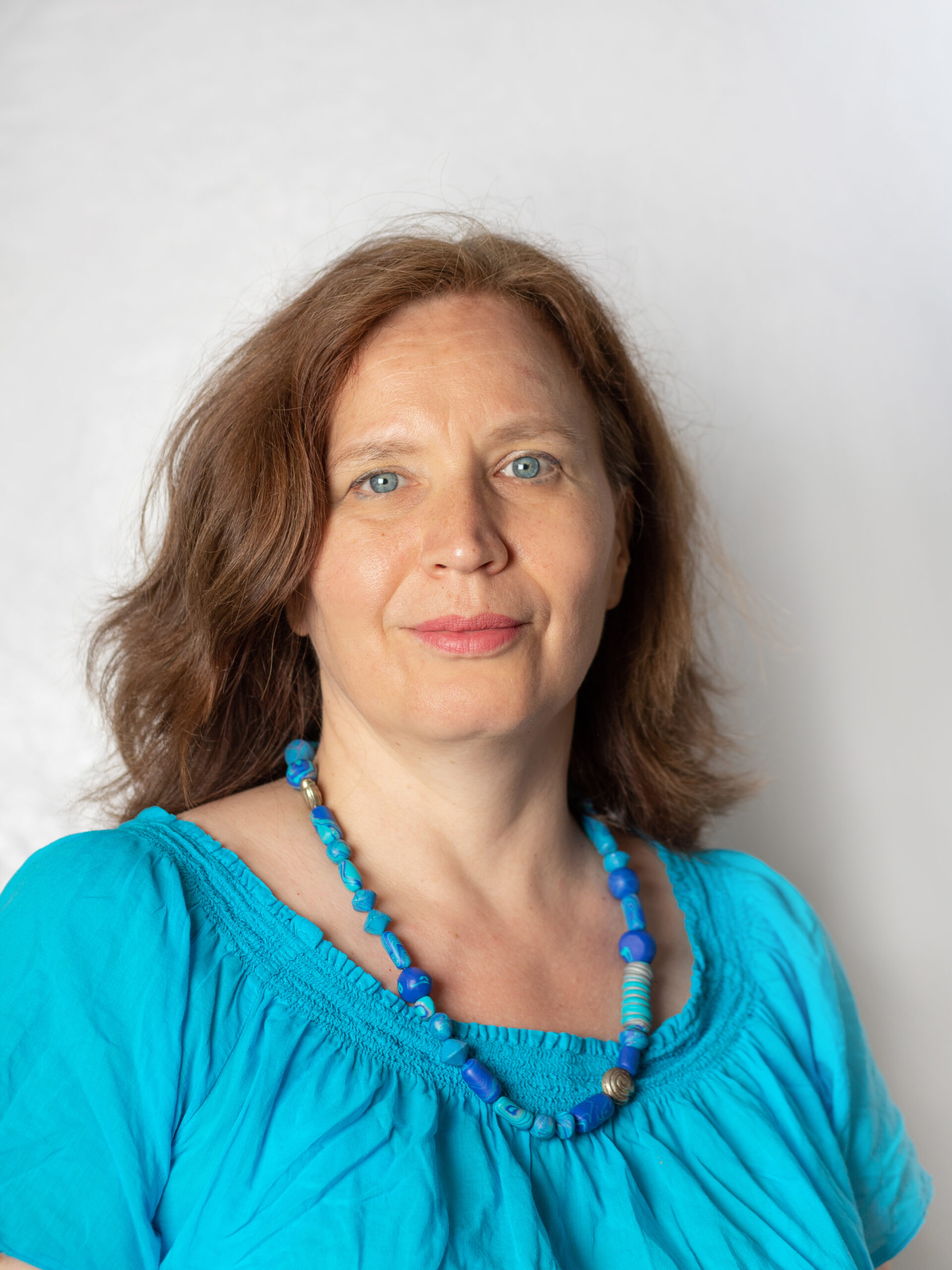 Frau mit langem, hellbraunem Haar. Sie trägt eine blaue Bluse und blaue Halskette.