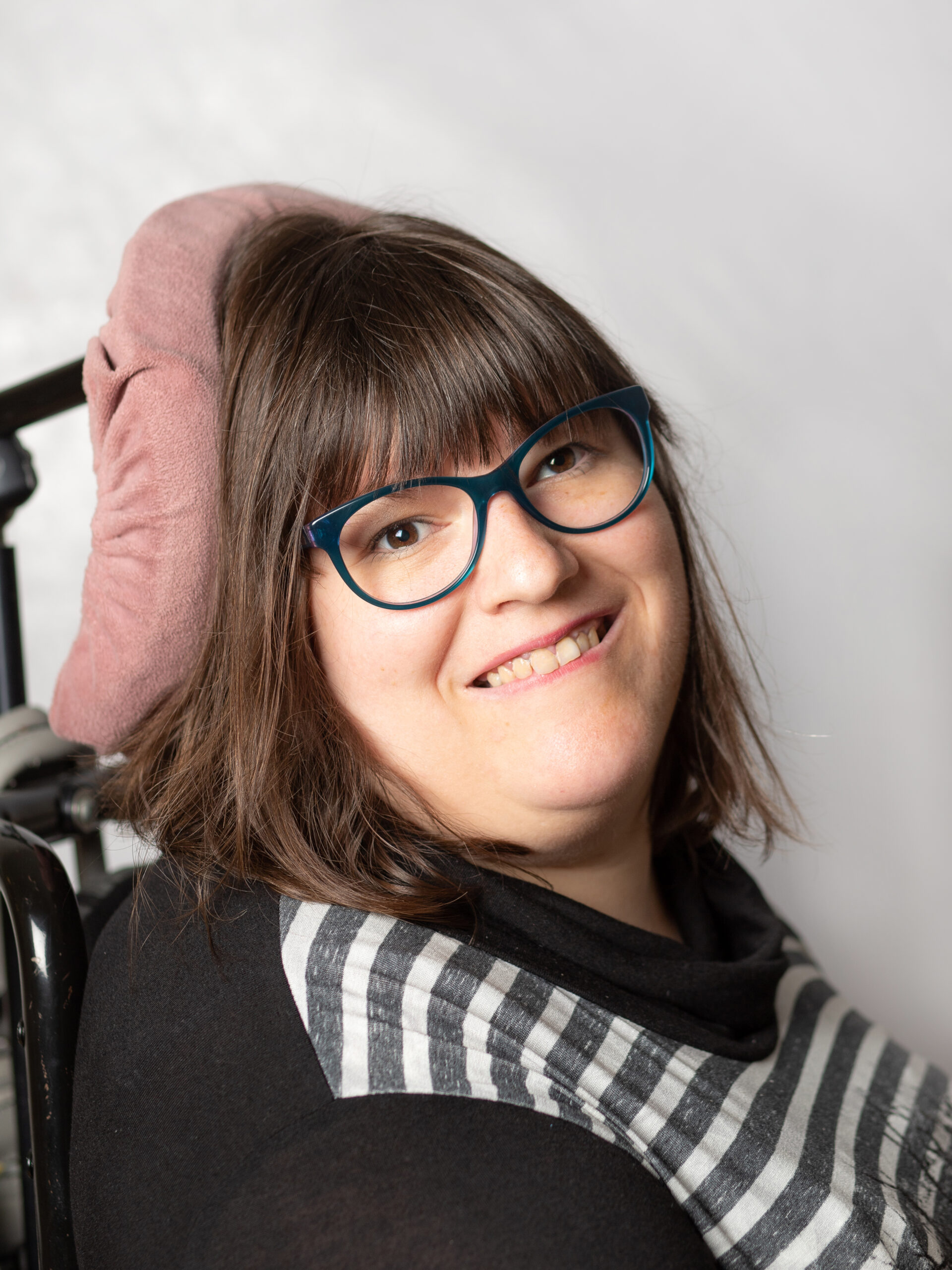 Lächelnde Frau mit Brille. Sie hat längeres, braunes Haar. Im Hintergrund eine Kopfstütze.