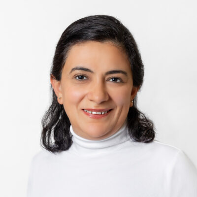 Frau mit schulterlangem dunkelbraunen Haar und weißem Rollkragen-Oberteil lächelt in die Kamera