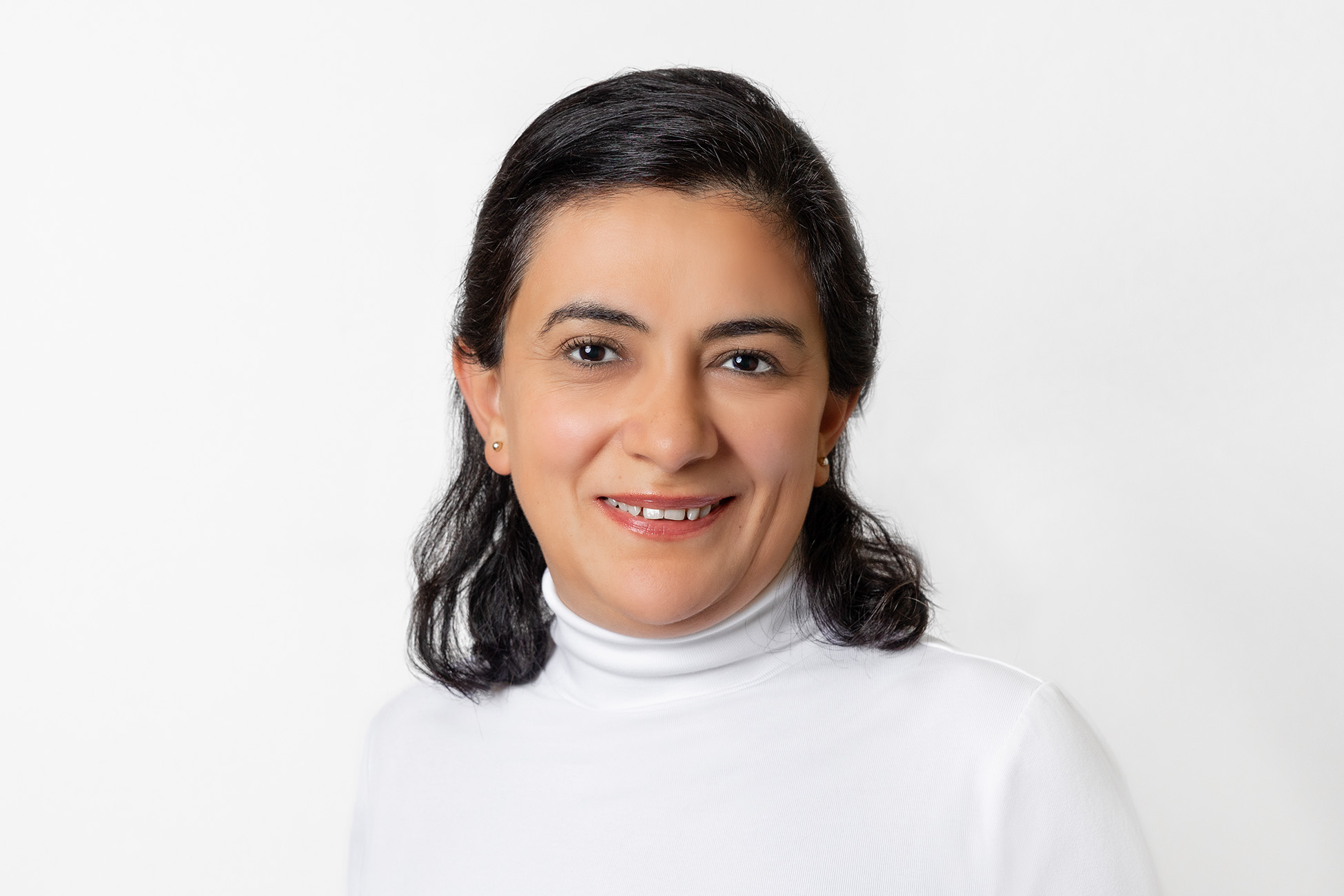 Frau mit schulterlangem dunkelbraunen Haar und weißem Rollkragen-Oberteil lächelt in die Kamera