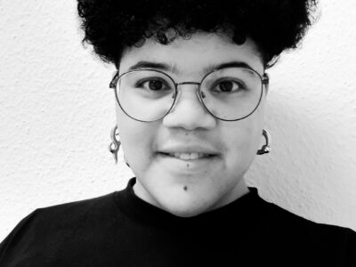 Person mit kurzem dunklem Haar und Brille.