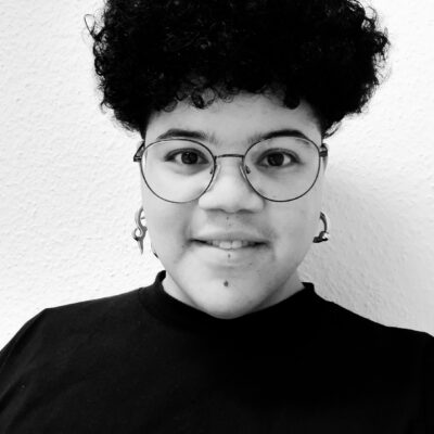 Person mit kurzem dunklem Haar und Brille.