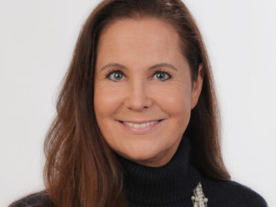 Frau mit langem, braunem Haar lächelt in die Kamera.