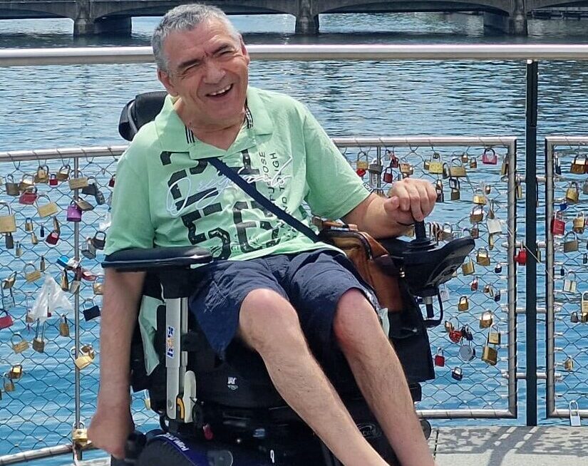 Mann im Rollstuhl auf einer Brücke mit sehr vielen "Liebesschlössern".