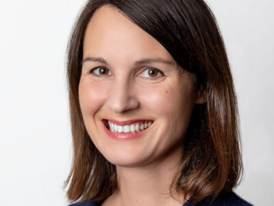 Frau mit schulterlangem Haar und Seitenscheitel lächelt in die Kamera