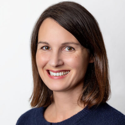 Frau mit schulterlangem Haar und Seitenscheitel lächelt in die Kamera