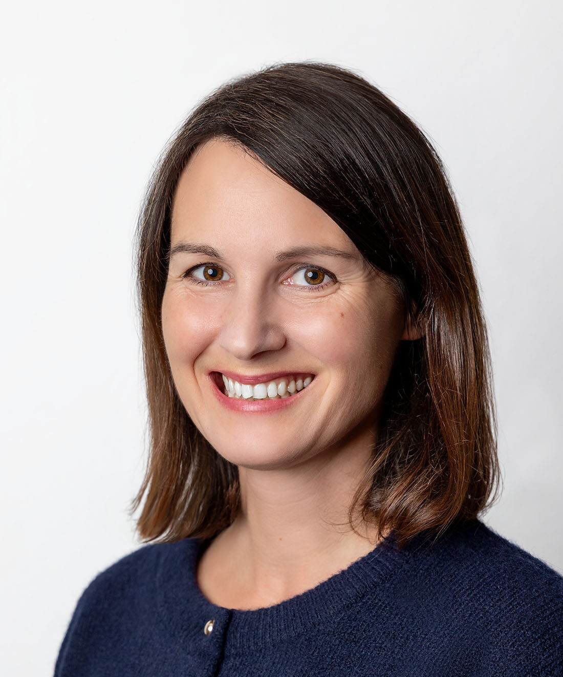 Frau mit schulterlangem Haar und Seitenscheitel lächelt in die Kamera