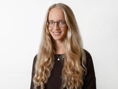 Frau mit langem blonden Haar und Brille lächelt in die Kamera