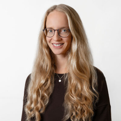 Frau mit langem blonden Haar und Brille lächelt in die Kamera