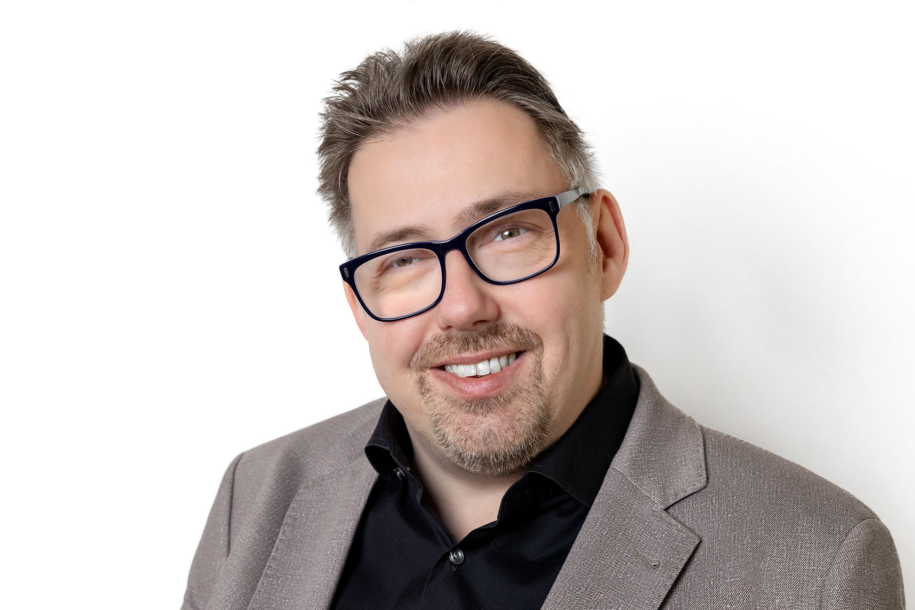 Mann trägt schwarze Brille und einen grauen Anzug. Er lächelt freundlich in die Kamera.