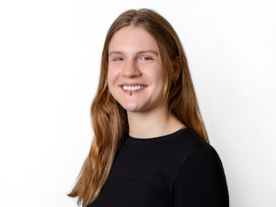 Frau mit brünetten, langen Haaren lächelt in die Kamera. Sie trägt ein Piercing.