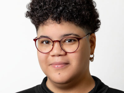 Person mit kurzem lockigen Haar und Brille lächelt in die Kamera