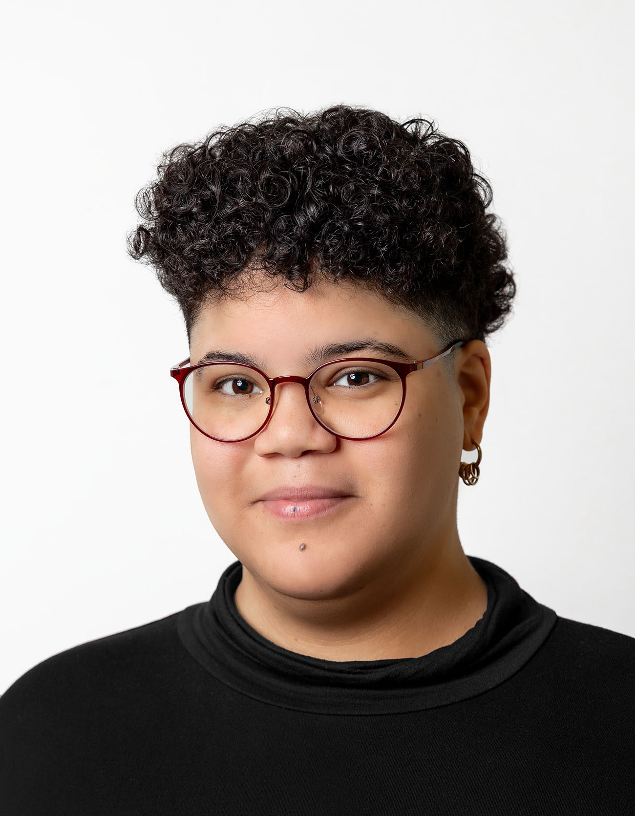 Person mit kurzem lockigen Haar und Brille lächelt in die Kamera