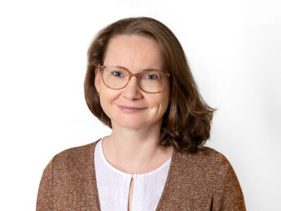 Frau mit schulterlangem braunen Haar und Brille schaut in die Kamera.