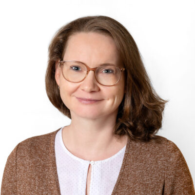 Frau mit schulterlangem braunen Haar und Brille schaut in die Kamera.