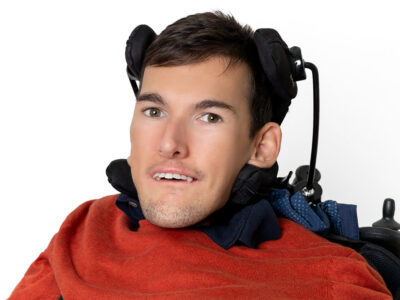 Mann mit kurzem braunen Haar trägt einen orangen Pullover und lächelt in die Kamera