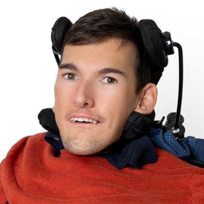 Mann mit kurzem braunen Haar trägt einen orangen Pullover und lächelt in die Kamera