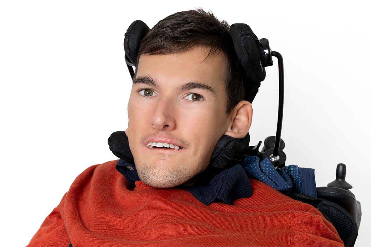 Mann mit kurzem braunen Haar trägt einen orangen Pullover und lächelt in die Kamera