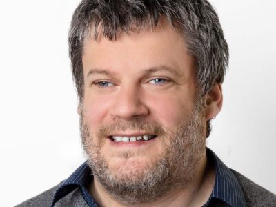 Mann mit graumeliertem kurzen Haar und Bart lächelt in die Kamera