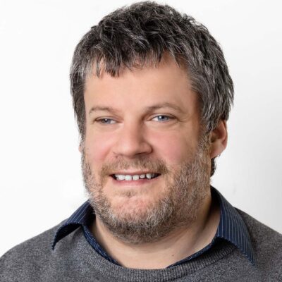 Mann mit graumeliertem kurzen Haar und Bart lächelt in die Kamera