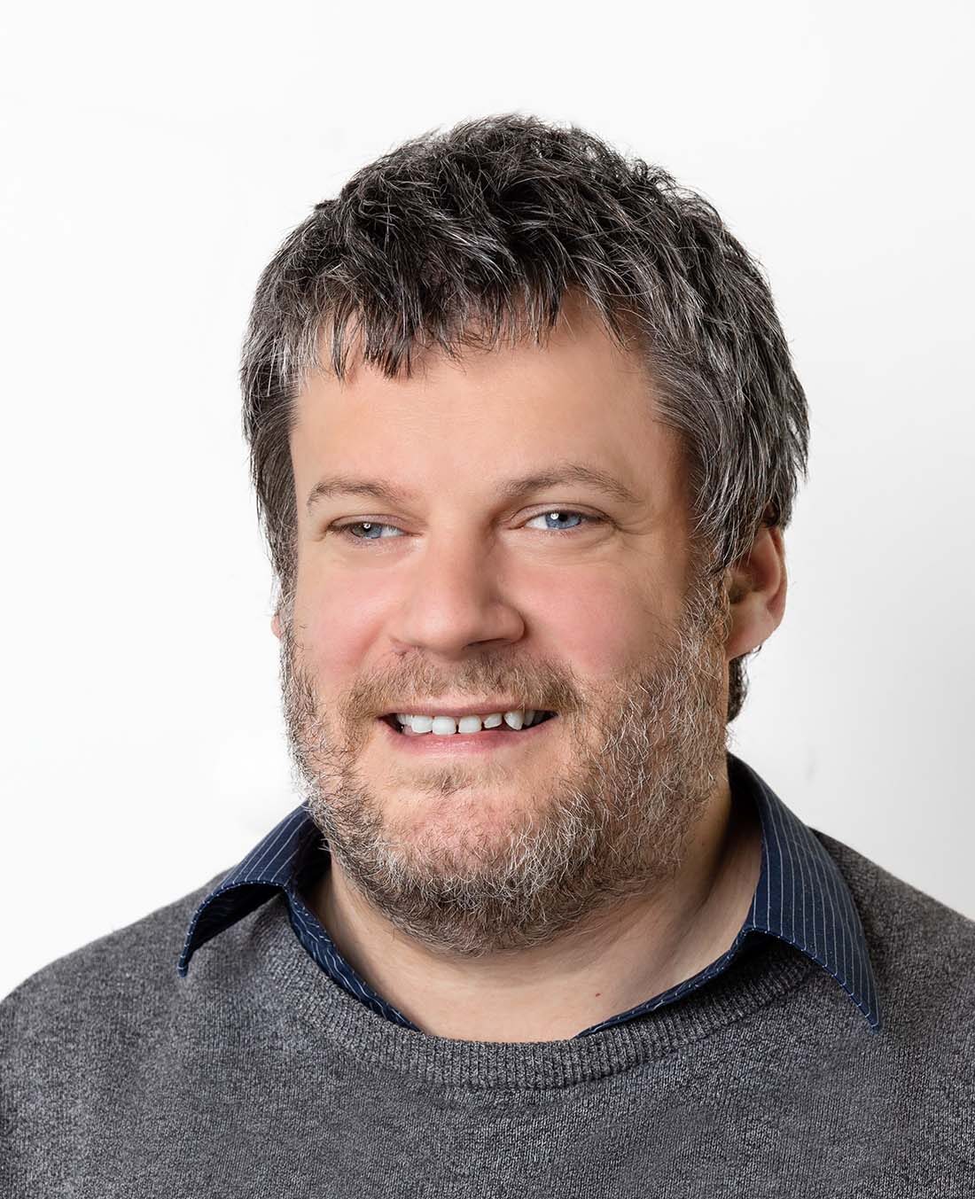 Mann mit graumeliertem kurzen Haar und Bart lächelt in die Kamera