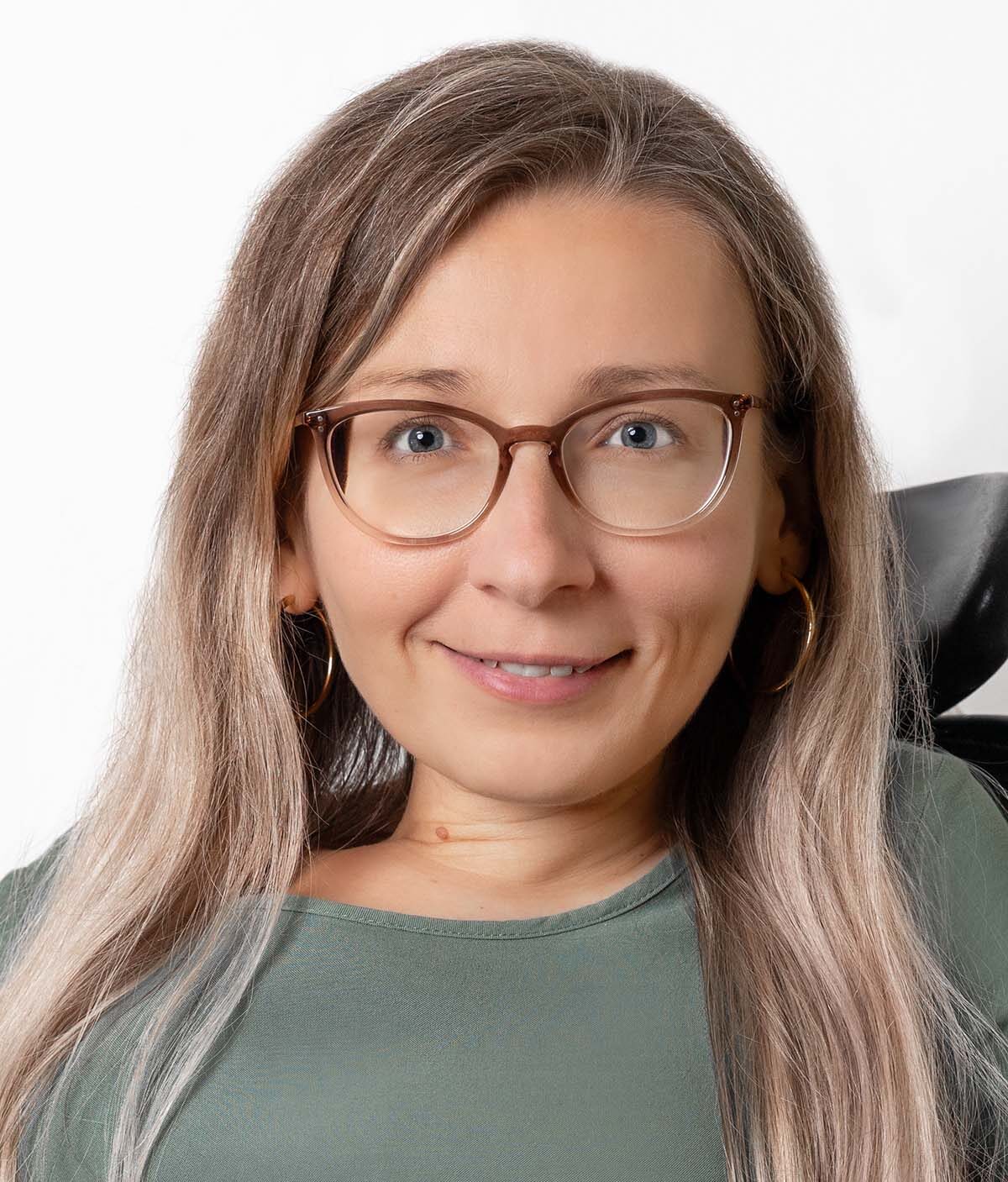 Frau mit langem Haar trägt eine Brille und lächelt freundlich in die Kamera