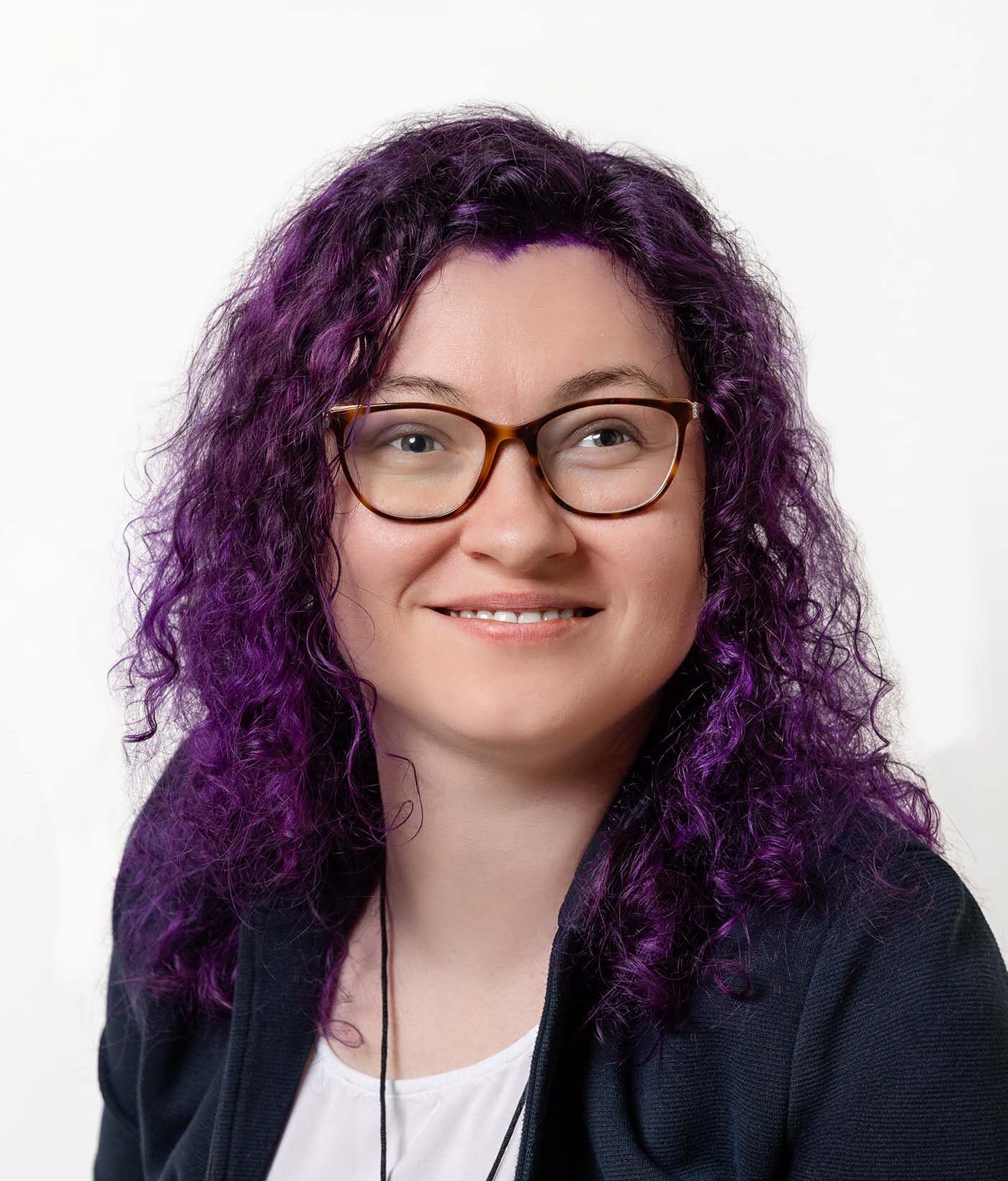Frau mit dunklem, leicht violettem Haar. Sie trägt Brille.
