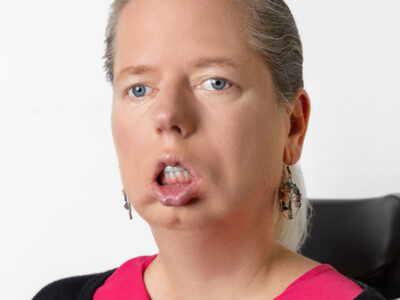 Frau mit blondem Haar im Zopf trägt eine pinke Bluse