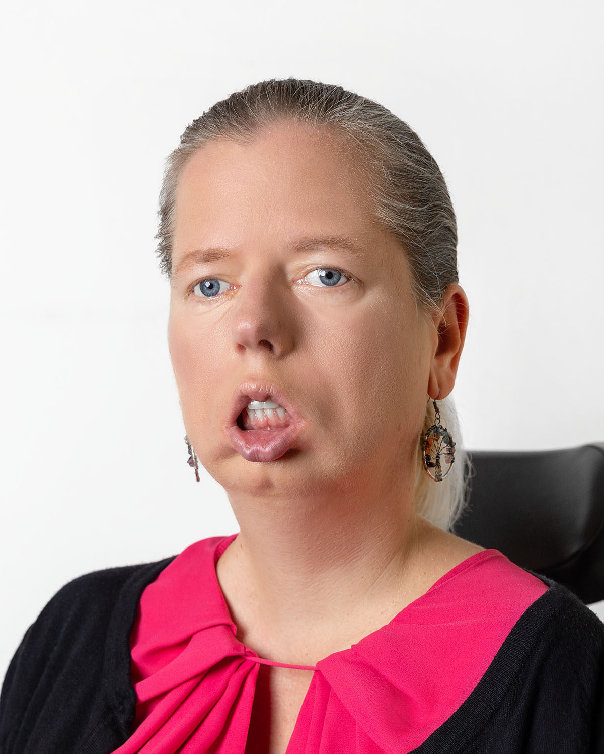 Frau mit blondem Haar im Zopf trägt eine pinke Bluse