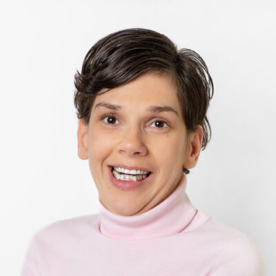 Frau mit kurzem, braunem Haar lächelt in die Kamera.