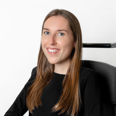 Frau mit braunem langen Haar und schwarzem Oberteil lächelt in die Kamera