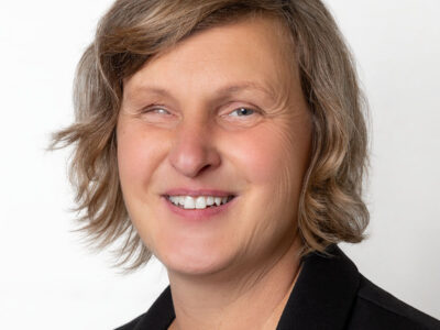 Frau mit brünettem, schulterlangen Haar lächelt in die Kamera