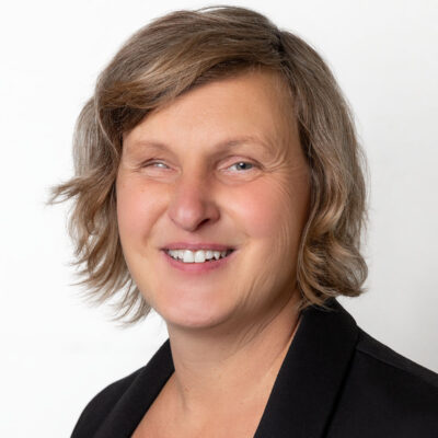 Frau mit brünettem, schulterlangen Haar lächelt in die Kamera