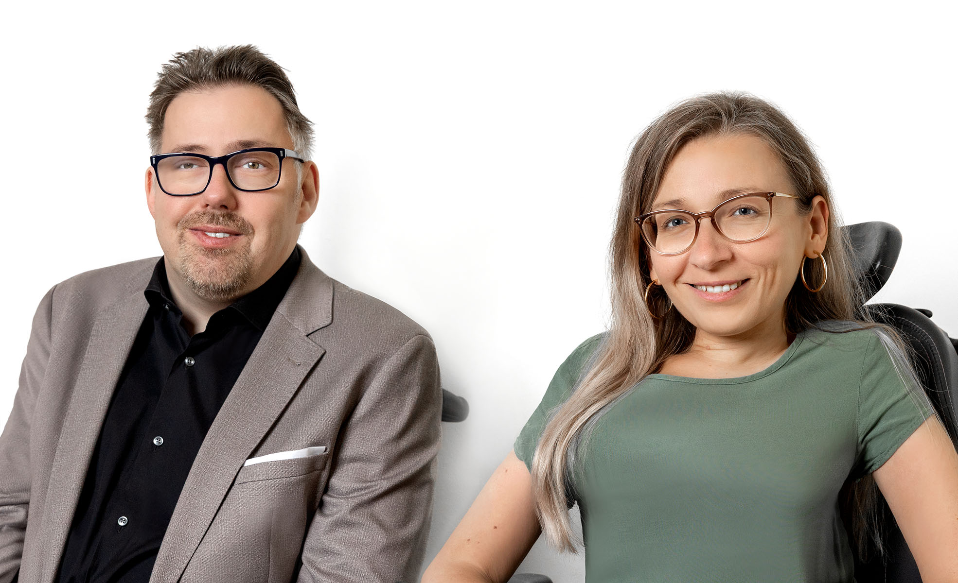 Eine Frau und ein Mann lächeln in die Kamera. Die Frau hat lange, blonde Haare, der Mann dunkles, kurzes Haar. Beide tragen eine Brille.